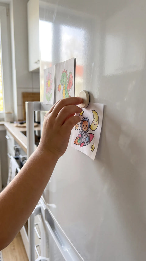 Ein Kind hängt sein bunt gestaltetes Motiv mit einem Magneten an den Kühlschrank.