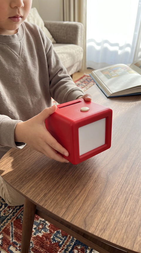 Ein Kind hält den roten Fantasini-Kreativdrucker mit beiden Händen am Tisch.